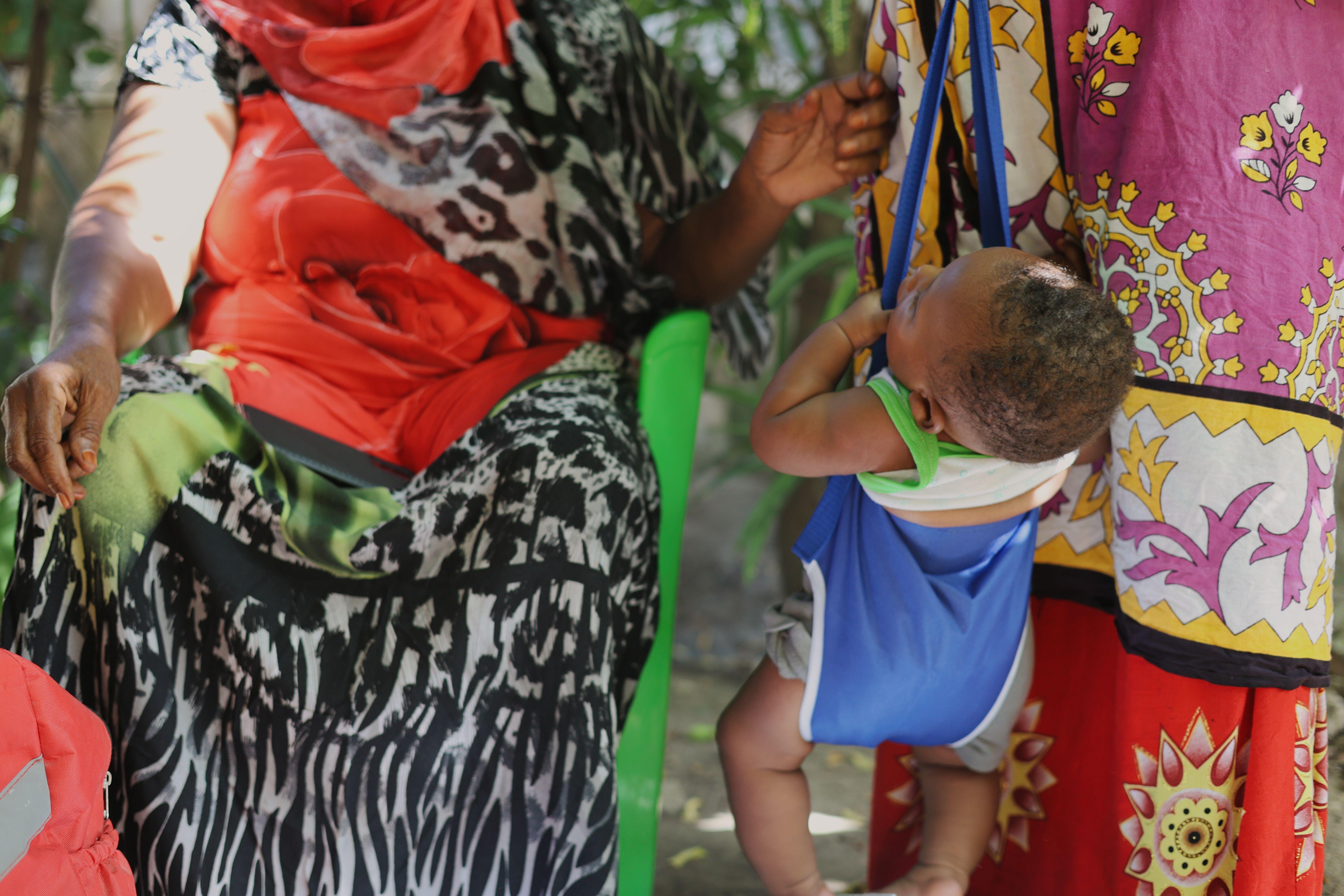  An infant in a blue sling scale is weighed during a home visit in Kilifi County, Kenya, while community health worker Mwanamkasi Hassan sits beside the child's mother.